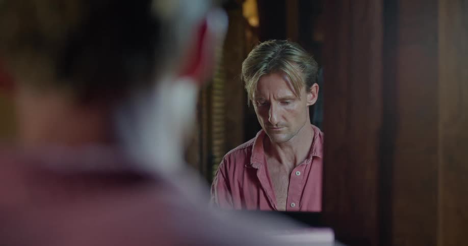Blonde man with pink shirt works on laptop in front of mirror