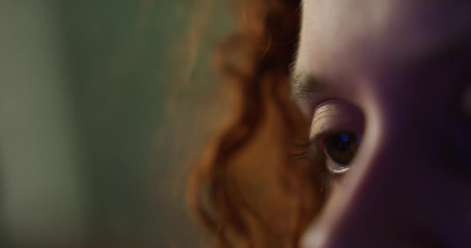 Close up of the eye of a redhead woman looking at a screen inside a room