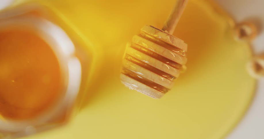 A wooden honey dipper above a pool of golden honey