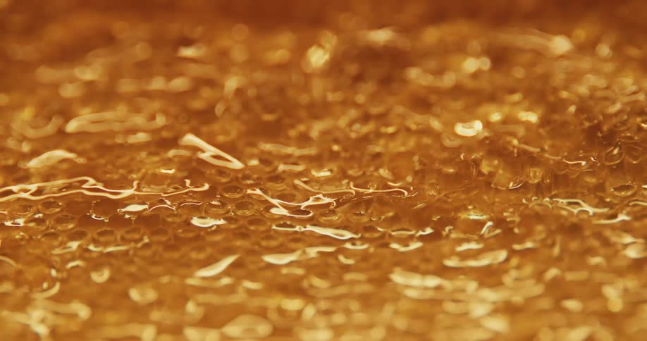 Amber golden honey drips as mass reflects lights