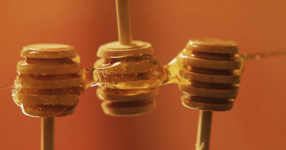 Honey dripping horizontally over honey dippers on a studio