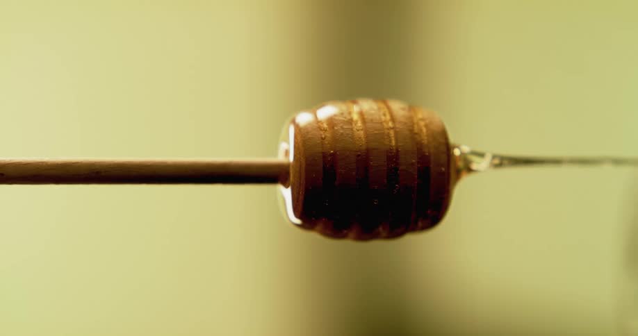 Honey flowing sideways from a wooden honey dipper