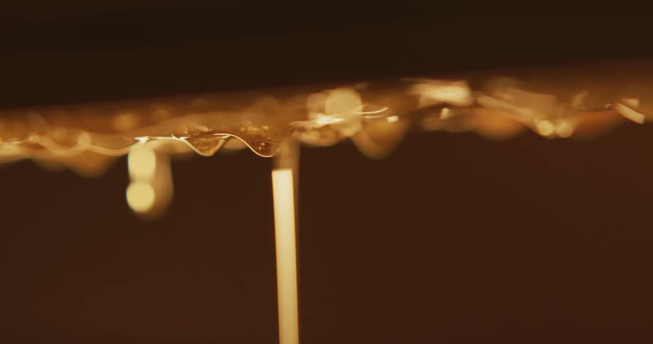 Honey drops off surface against a solid brown background