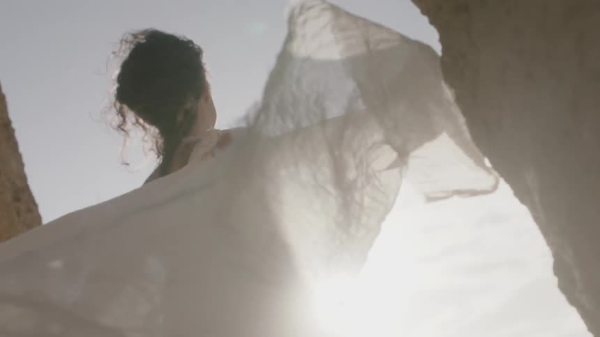 A woman in a white dress stands in the sunlight