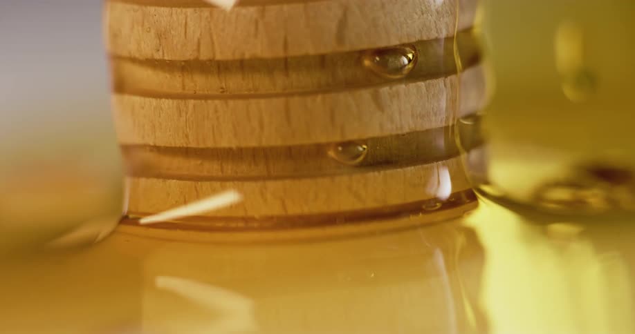 Amber honey pools around base of wooden utensil against a solid gray background