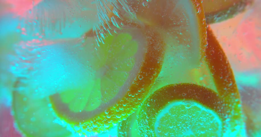 Ice cubes and orange slices sit together in clear liquid as tiny bubbles rise to the top