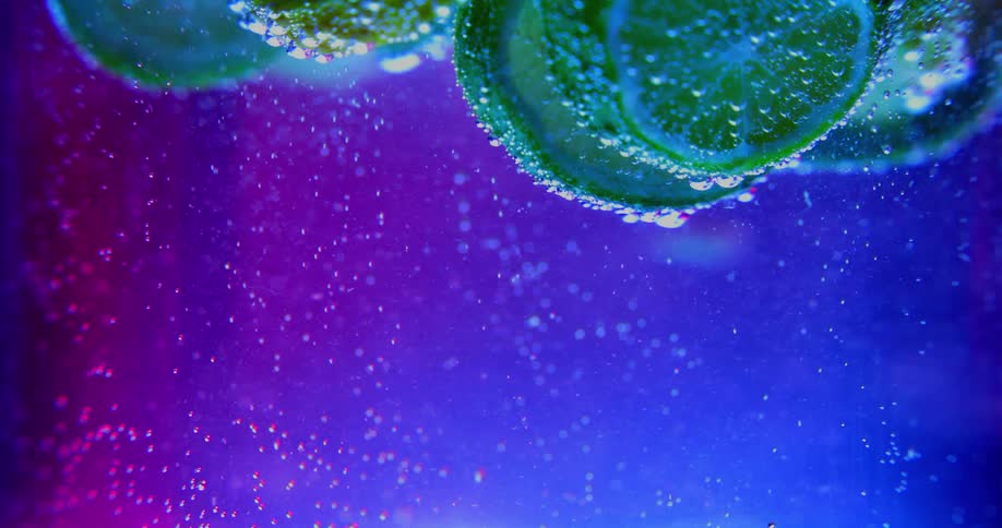 Air bubbles rising up a liquid covering the lemon and lime slices floating in the surface under a blue light