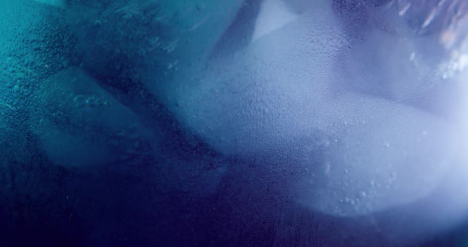 Liquid is shown with ice cubes in it as more liquid is then poured in and lots of bubbles rise to the surface
