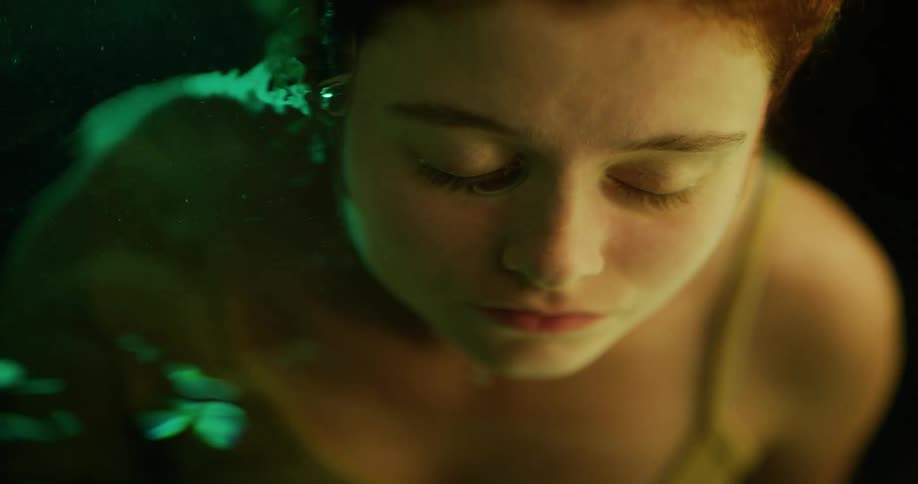 A woman with her eyes closed and face submerged in a pool of water lifts her head