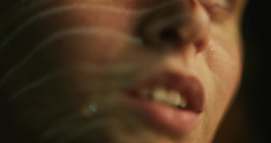 Water reflecting face of woman ripples as drops fall onto surface