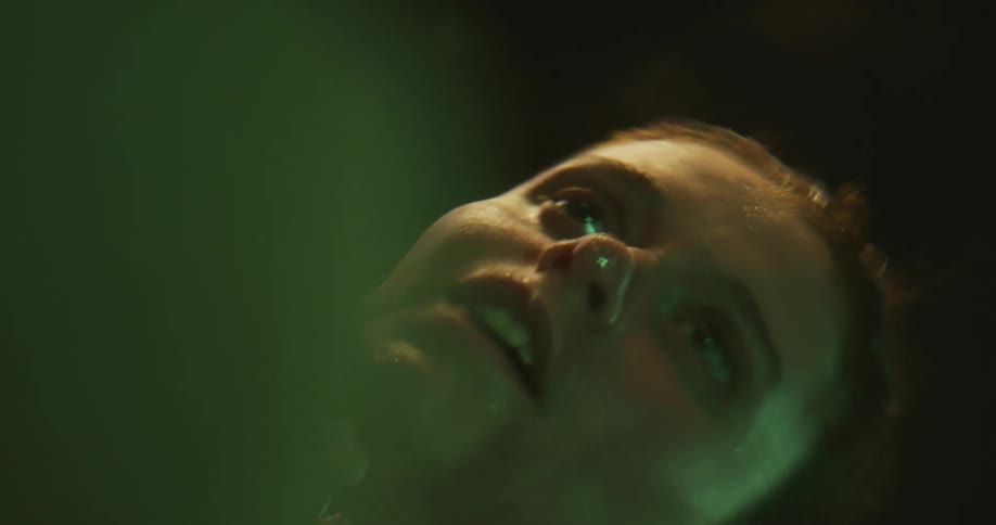 Young woman rubs her face while looking at her reflection on the surface of water