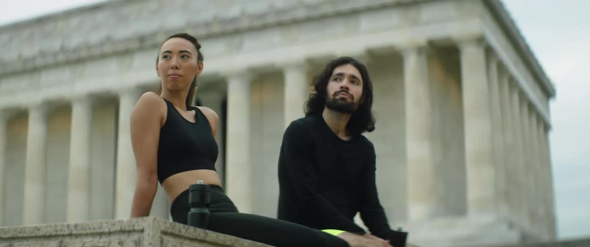 A man and woman sit on a ledge outside a national monument