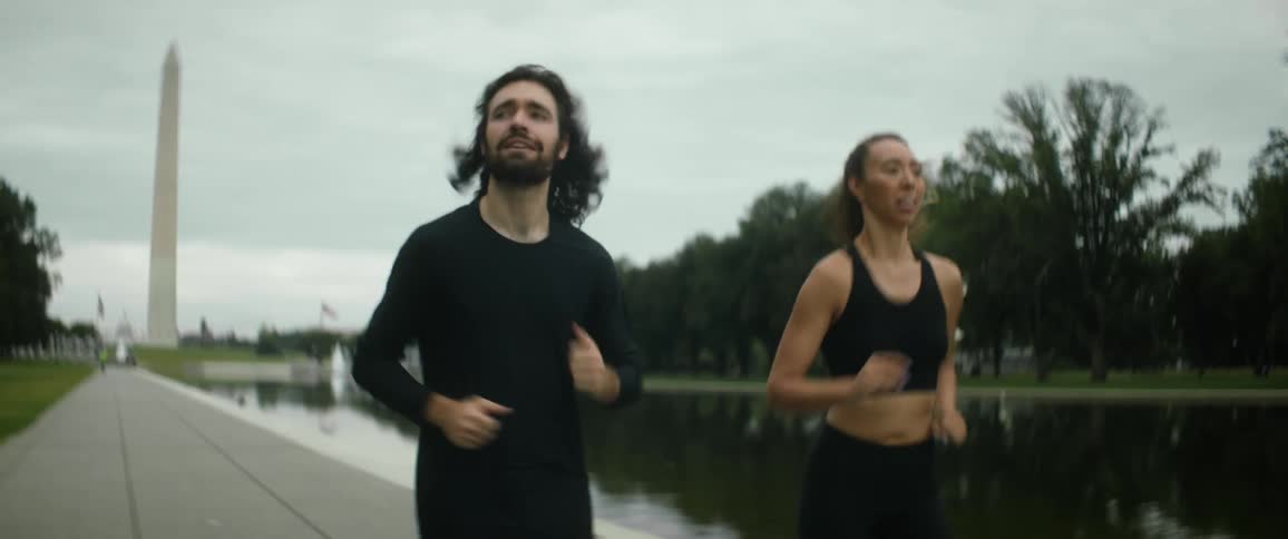 A man and woman jog next to a river in a public park