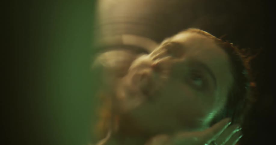 Young woman rubs her face while looking at her reflection on the surface of water