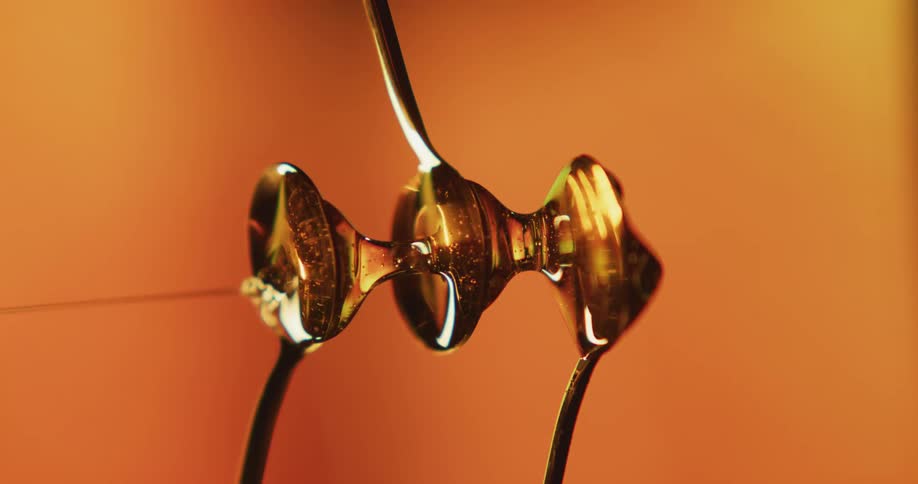 Spoons sitting one above the other with flowing honey are canted to show drops moving horizontally