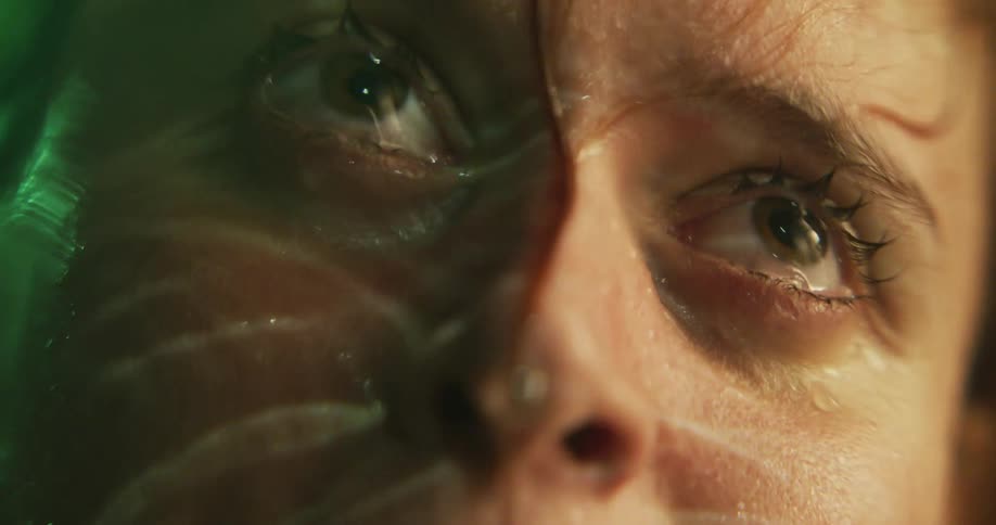 Rippling water reflects face partly lit by green lighting