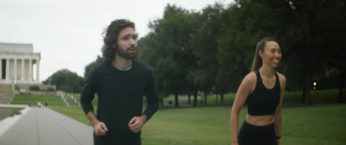 Woman with ponytail black sports bra and man with long wavy hair and black sweater start running next to lincoln memorial reflecting pool