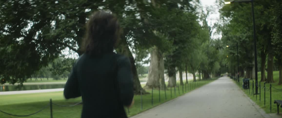 Man with long hair jogs on a path on a park near a lake at daytime