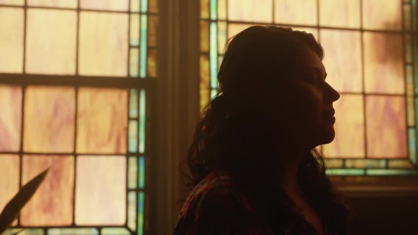 Silhouette of a woman praying with her eyes closed near a window on a church