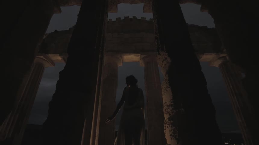 A woman in a toga stands near pillars at night