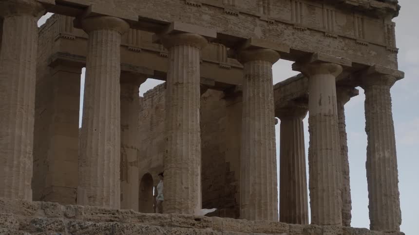 A woman is walking past pillars on a cloudy day