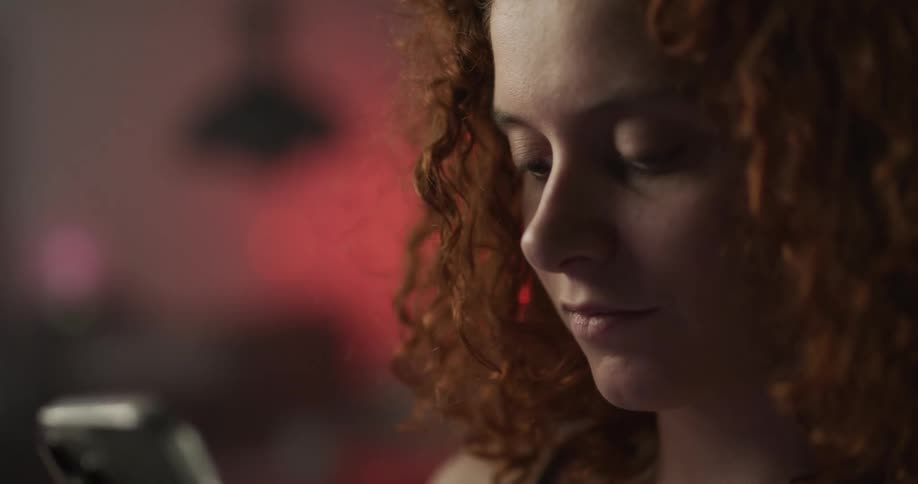 Redheaded woman smiles slightly while tapping on a smartphone