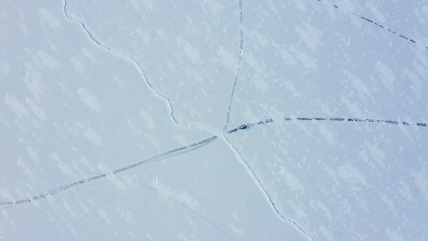 Vehicle moves along road cutting through snow covered plains