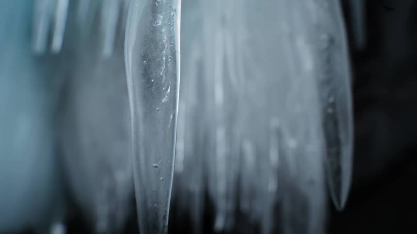 Close up of pointy icicles hanging from the roof inside a dark aera