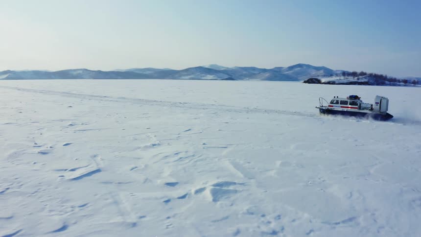 A hoovercraft is traveling across the snow covered ice and there are snow covered mountains in the distance