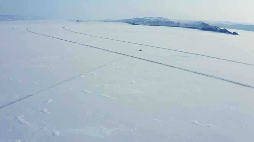 Aerial view of a hovercraft driving over the snow on an arctic landscape near the mountains