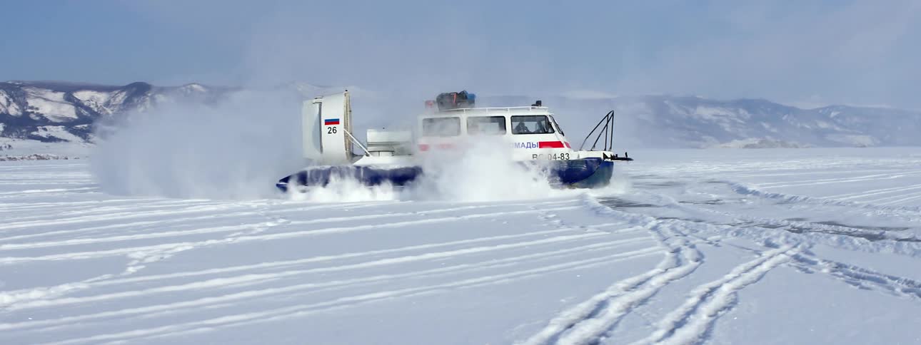 A hovercraft is traveling across the snow covered ice and snow flies as it slides and turns
