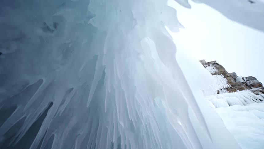 Icicles are hanging from a cliff among mountains and rock formations