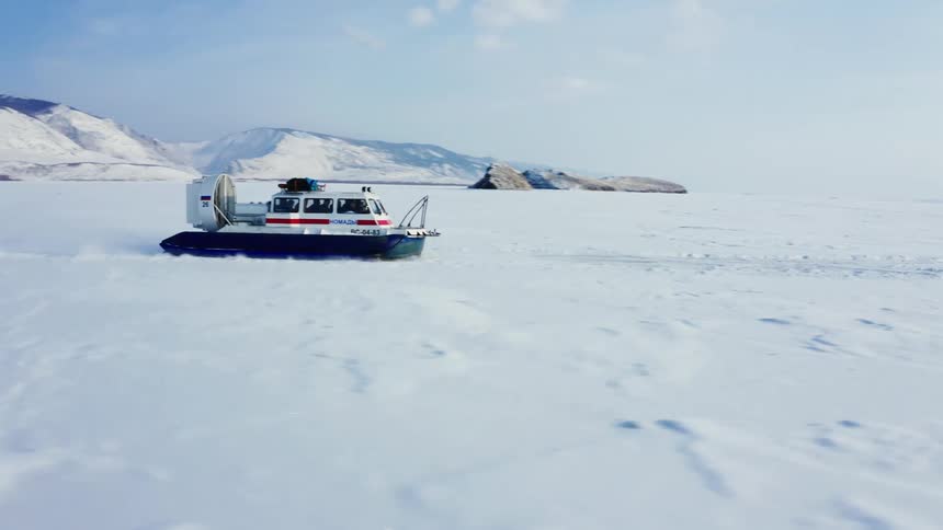 A hoover craft is traveling across the snow covered ice and there are snow covered mountains in the distance