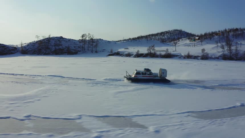 A hovercraft is traveling across the snow covered ice and there are snow covered mountains in the distance