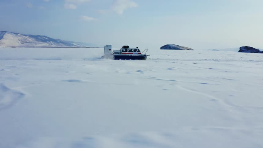 Large hovercraft moves over ice and snow covered plain with mountains in the background