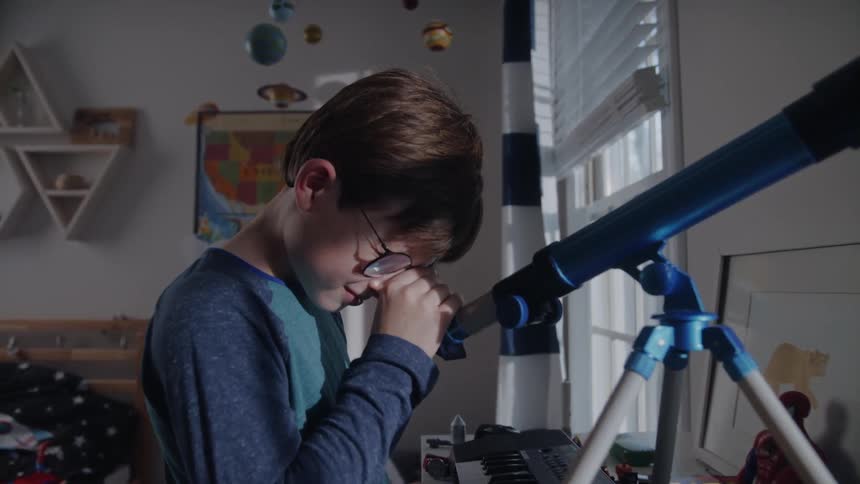 Kid stands looking into telescope sitting on his table