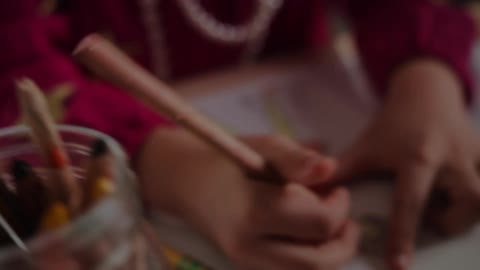 A little girl colors a picture of a woman wearing a dress with colored pencils
