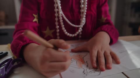 A young girl colors a drawing on a sheet of paper while sitting at table indoors during the day