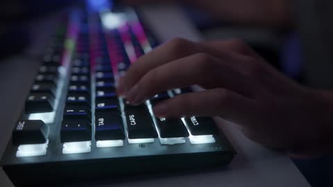 A person is typing on a computer keyboard that is illuminated with lights