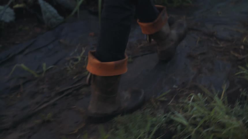 Person with black pants and a pair of brown shoes walks along muddy track