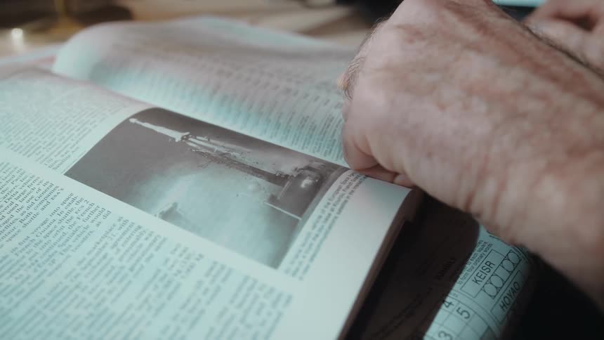 A man is reading a book that is sitting on the table in front of him and he moves his finger across the page