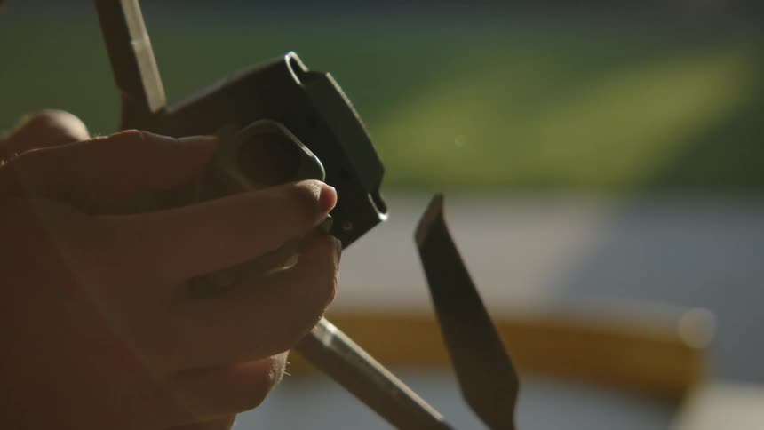 Close up of the hands of a man turning a drone upside down to check the camera at morning