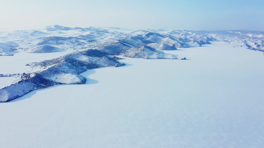 Aerial view of the frozen plains covered in snow next to a mountain range in the arctic