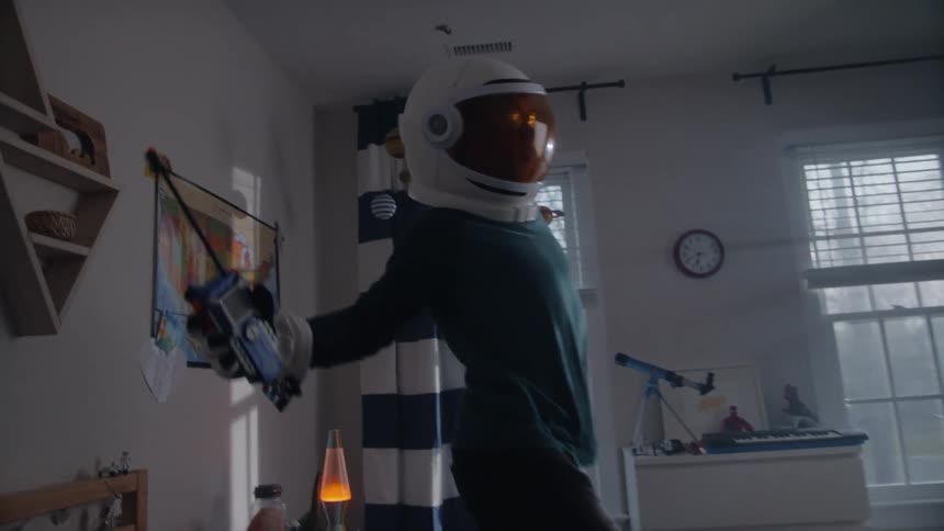 A boy wearing toy astronaut gear pretends to be walking on the moon while standing on his bed