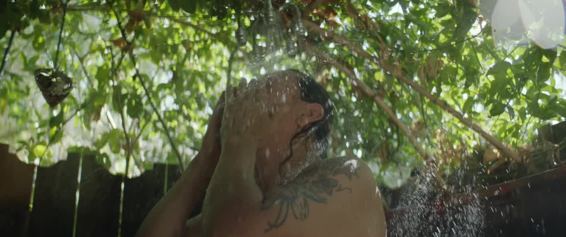 A man showers outdoors in a fenced area during the day