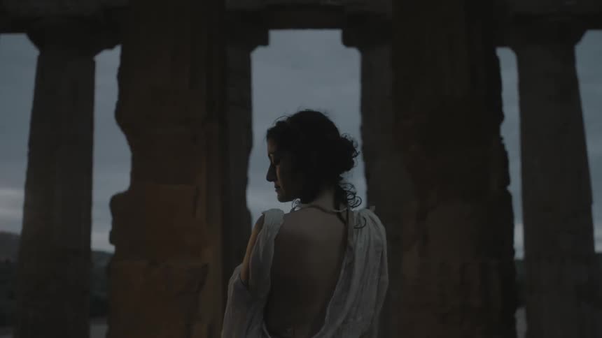 A woman standing near large rock columns in an evening breeze