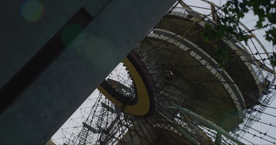 Birds fly over tower and nearby structure of cables with a central ring