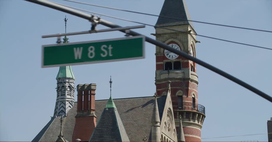 Moving through town a clocktower next to an old church is seen between traffic signals and buildings