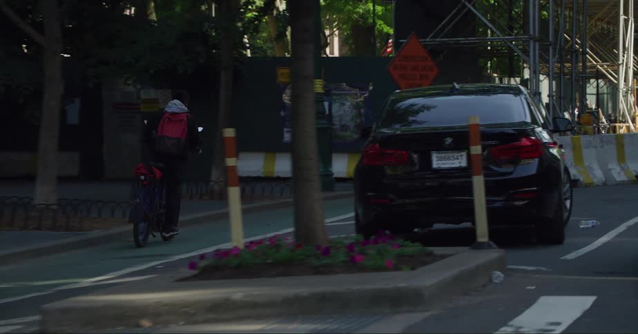 Cyclist rides along bike lane passing cars and pedestrians walking under construction scaffolding