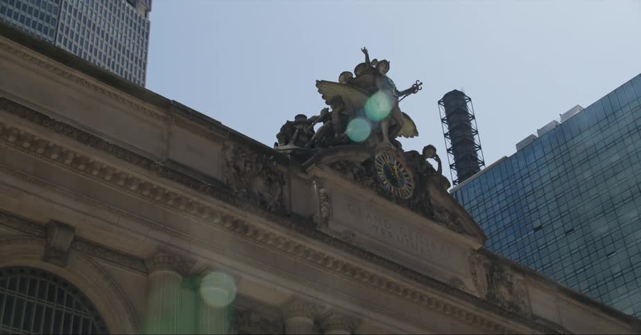A statue and clock on top of a city building with skyscrapers